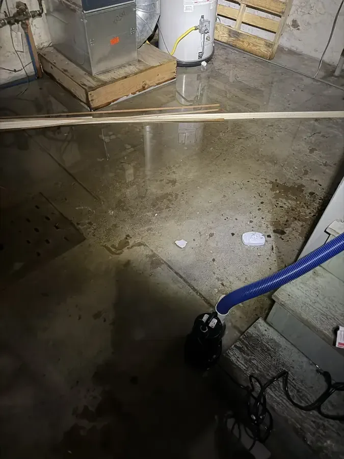 Extraction hose removing standing water from a concrete utility-room floor beside a water heater