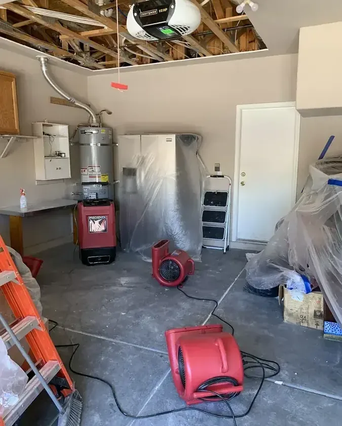 Air movers and a dehumidifier drying a garage with the ceiling opened after a water heater leak