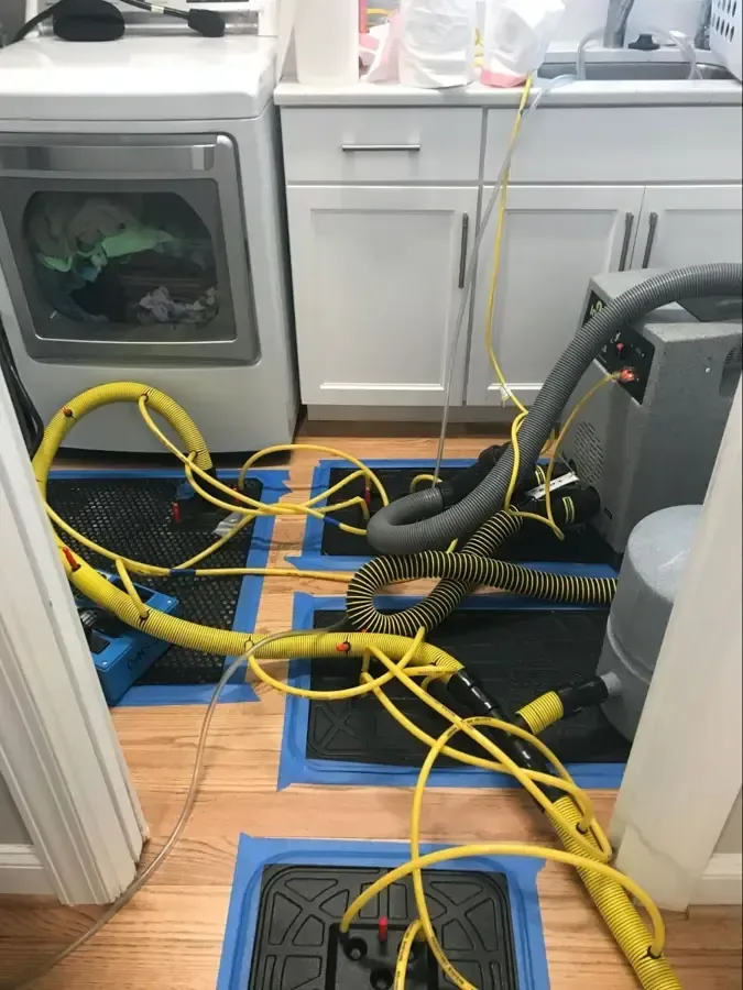 Floor drying mats and hoses set up in a laundry room after a washer leak