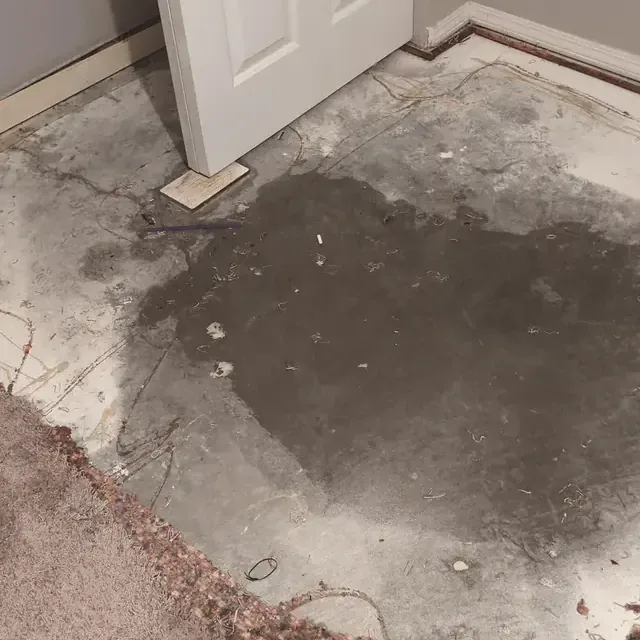 Dark damp patch across exposed concrete flooring beside a doorway